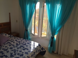 Une chambre à coucher avec un lit, une tête de lit en bois, une table de chevet et une fenêtre avec des rideaux.