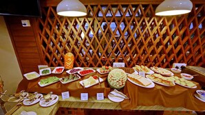 A buffet table with various food items and utensils, set against a wooden lattice backdrop. - Sanctuary Hotel (Mandalay)