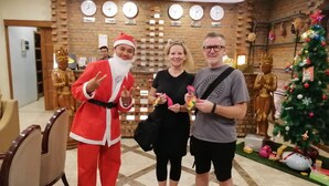 A lobby with a brick wall, clocks, a Christmas tree, and a statue. - Sanctuary Hotel (Mandalay)