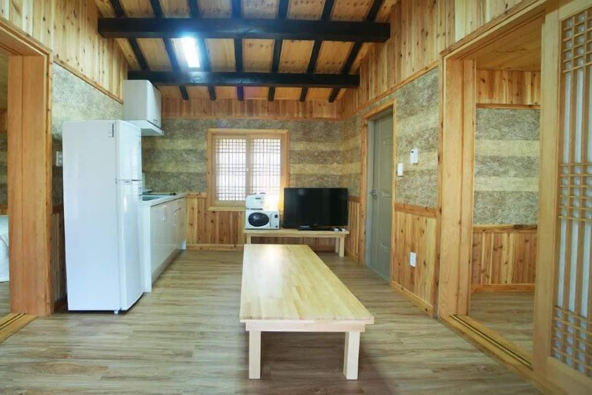 A wooden interior with a bed, a white refrigerator, a wooden table, and a television.