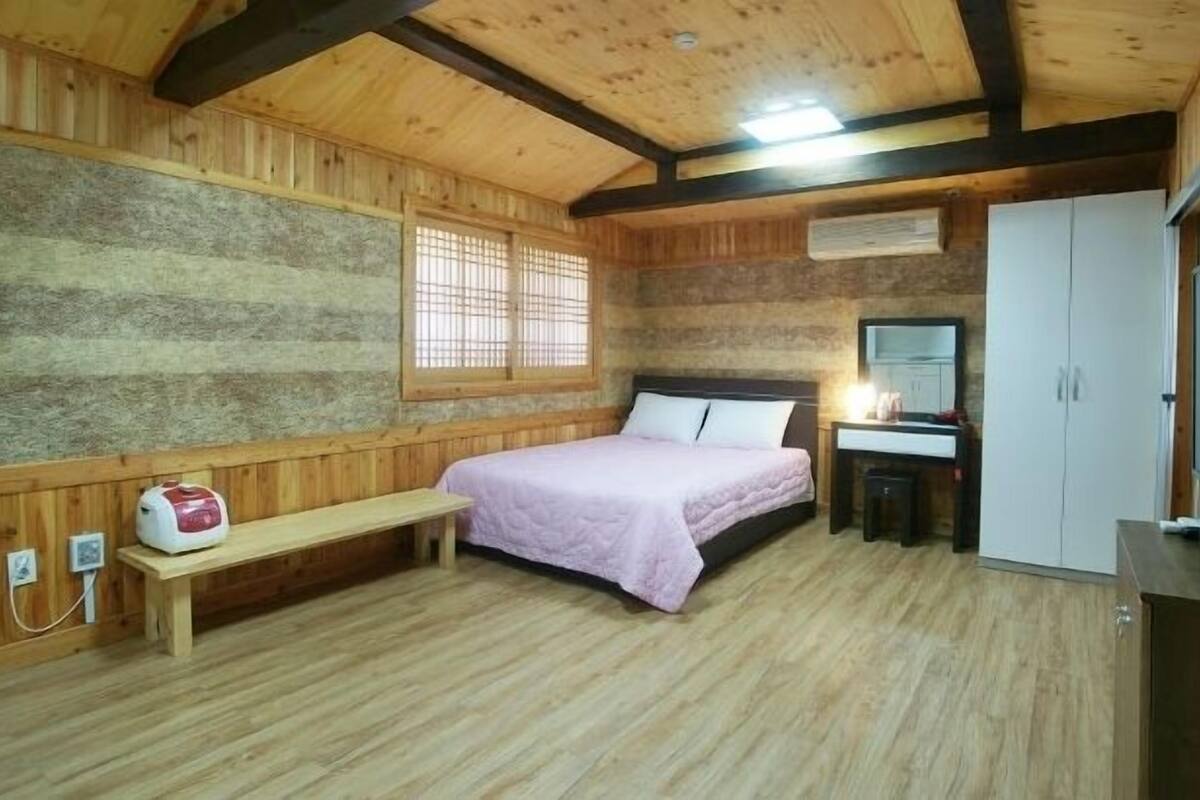 A wooden room with a bed, a bench, a desk, a mirror, and a wardrobe.