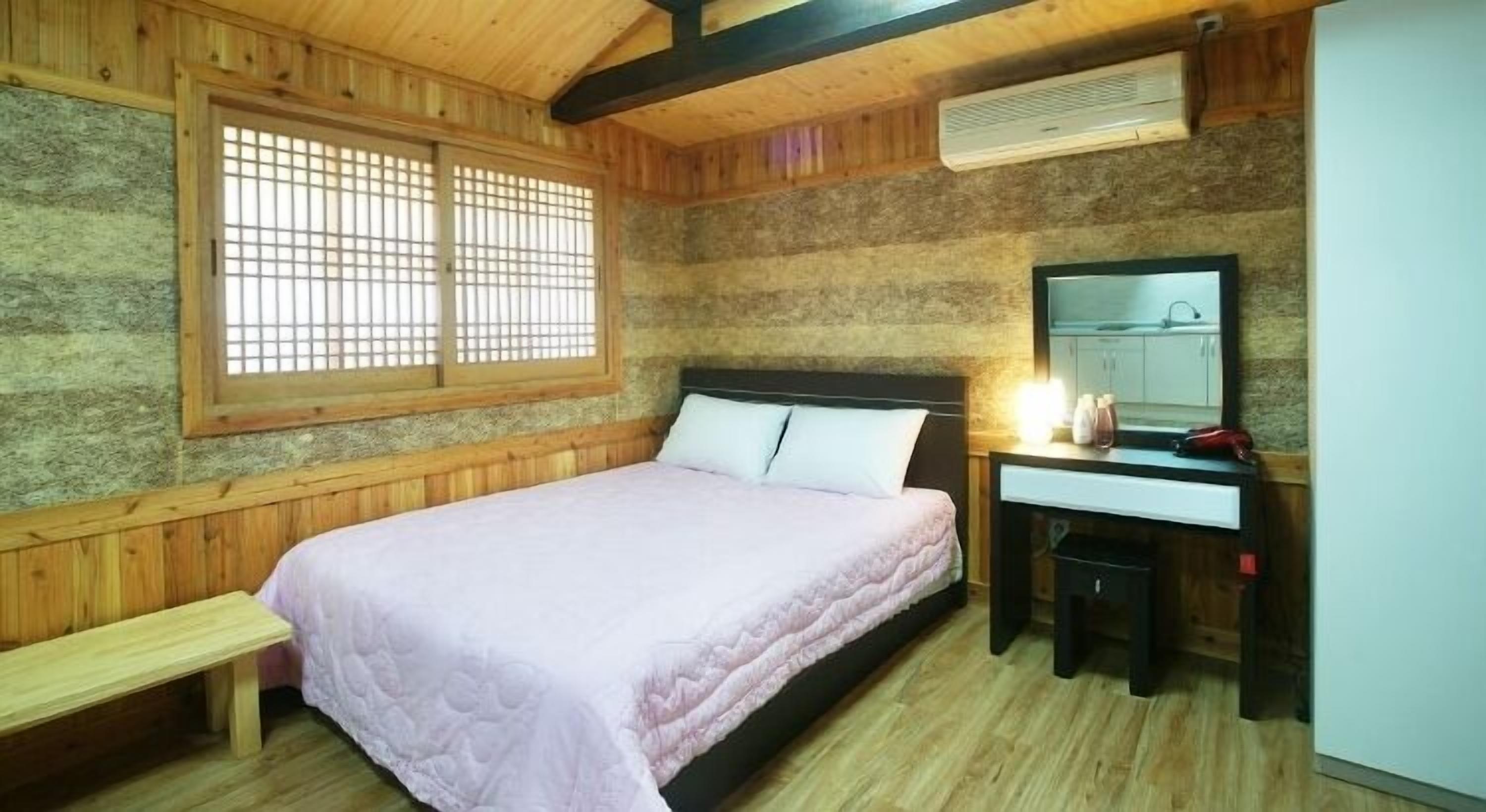 A bedroom with a bed, a bench, a desk with a mirror, and a window with wooden shutters.