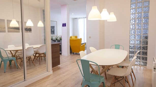 A modern dining area with a large white table, teal chairs, and pendant lights.