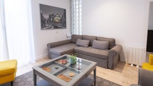 A modern living room with a grey sofa, a glass coffee table, and a cityscape painting on the wall.