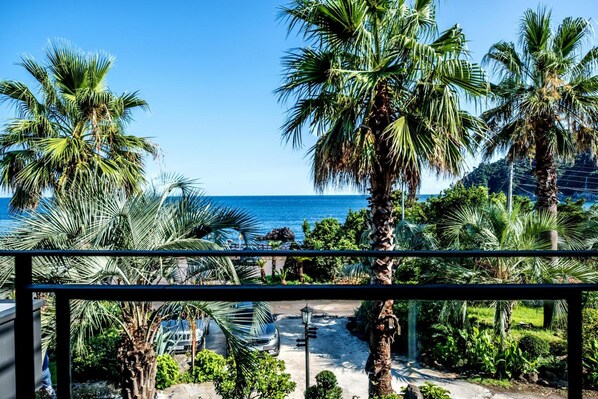 A view from a balcony overlooking a palm tree-lined pathway leading to a beach.