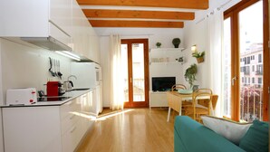 A compact kitchen with a toaster, kettle, and a red pot. There's a wooden dining table with chairs and a teal sofa. - Bright Studio in the heart of Palma with Balcony, Wifi, AC, Great for Couples (Palma)