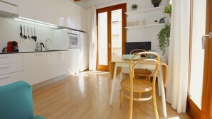 A modern kitchen with white cabinets, a dining table with chairs, and a wooden floor. - Bright Studio in the heart of Palma with Balcony, Wifi, AC, Great for Couples (Palma)