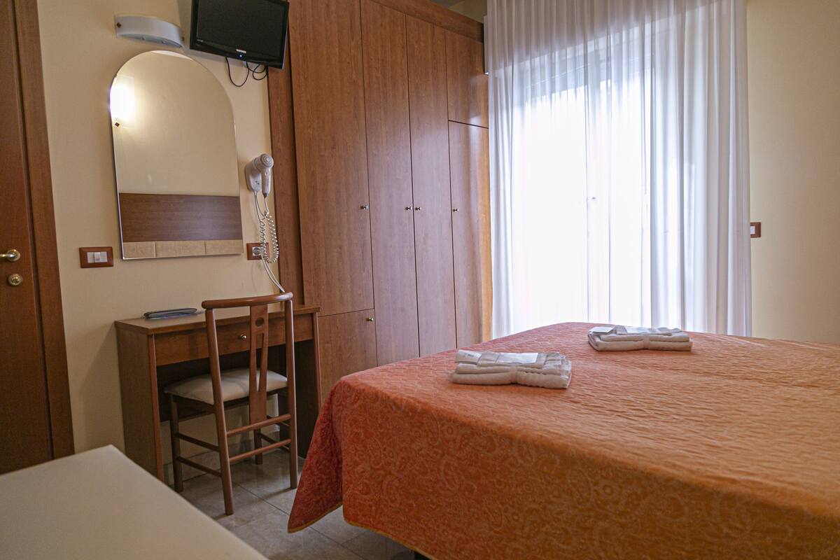 A hotel room with a bed, a desk, a chair, a hairdryer, and a television.