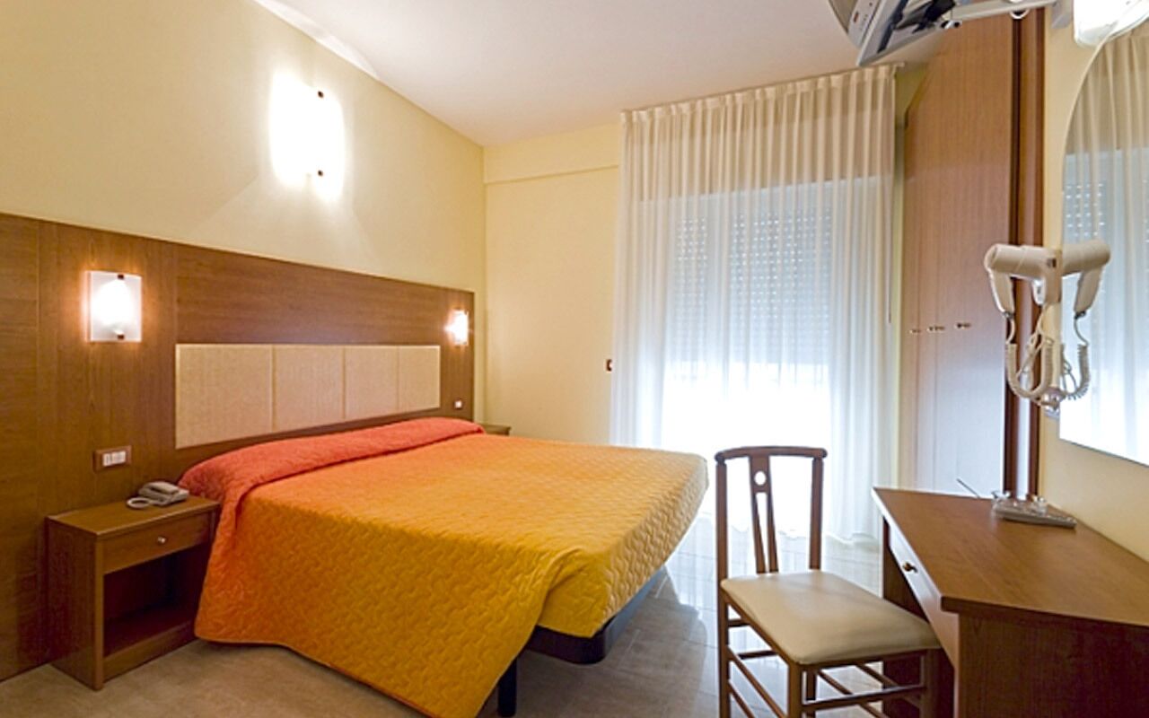 Una habitación de hotel con cama, mesita de noche, silla, escritorio y espejo.
