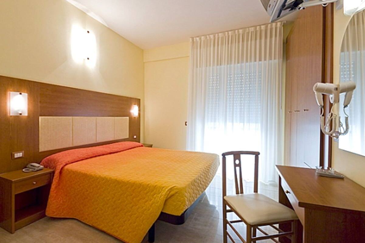A hotel room with a bed, bedside table, chair, desk, and a mirror.