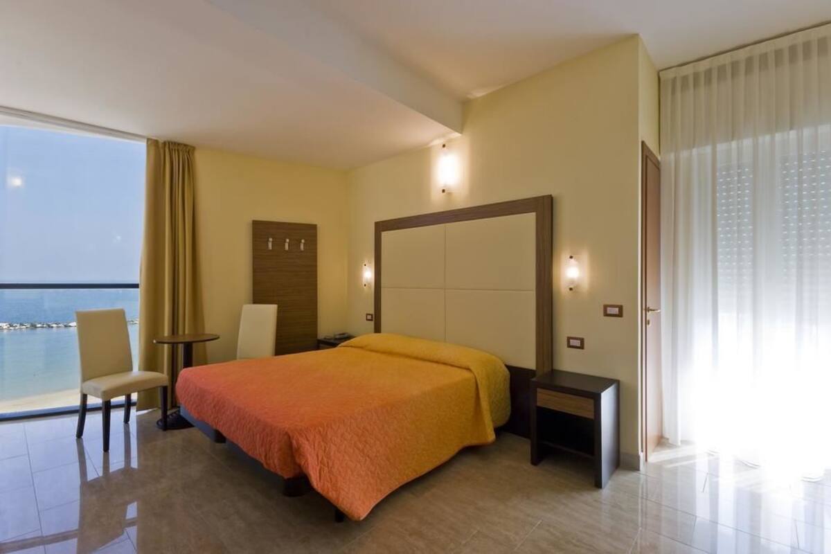 A hotel room with a large bed, a desk, a chair, and a view of the sea.