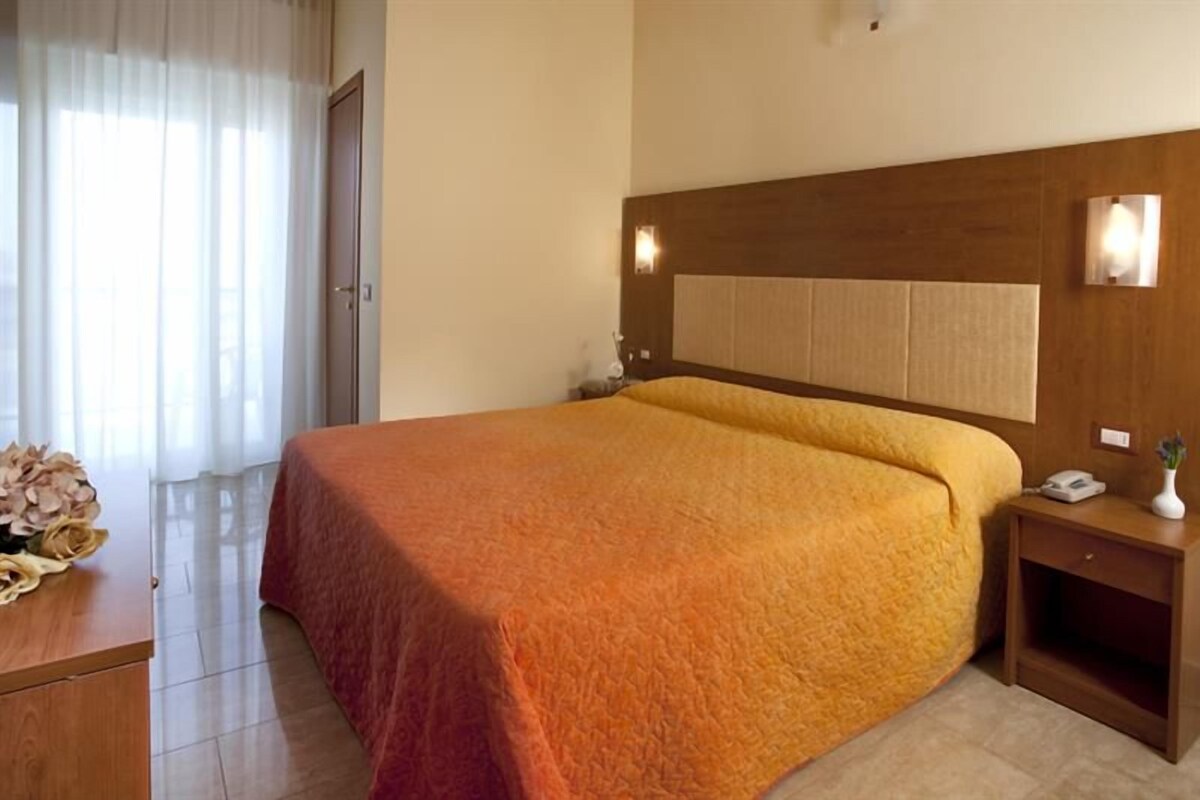 Habitación de hotel con una cama grande, una mesita de noche, una lámpara de pared y una puerta.