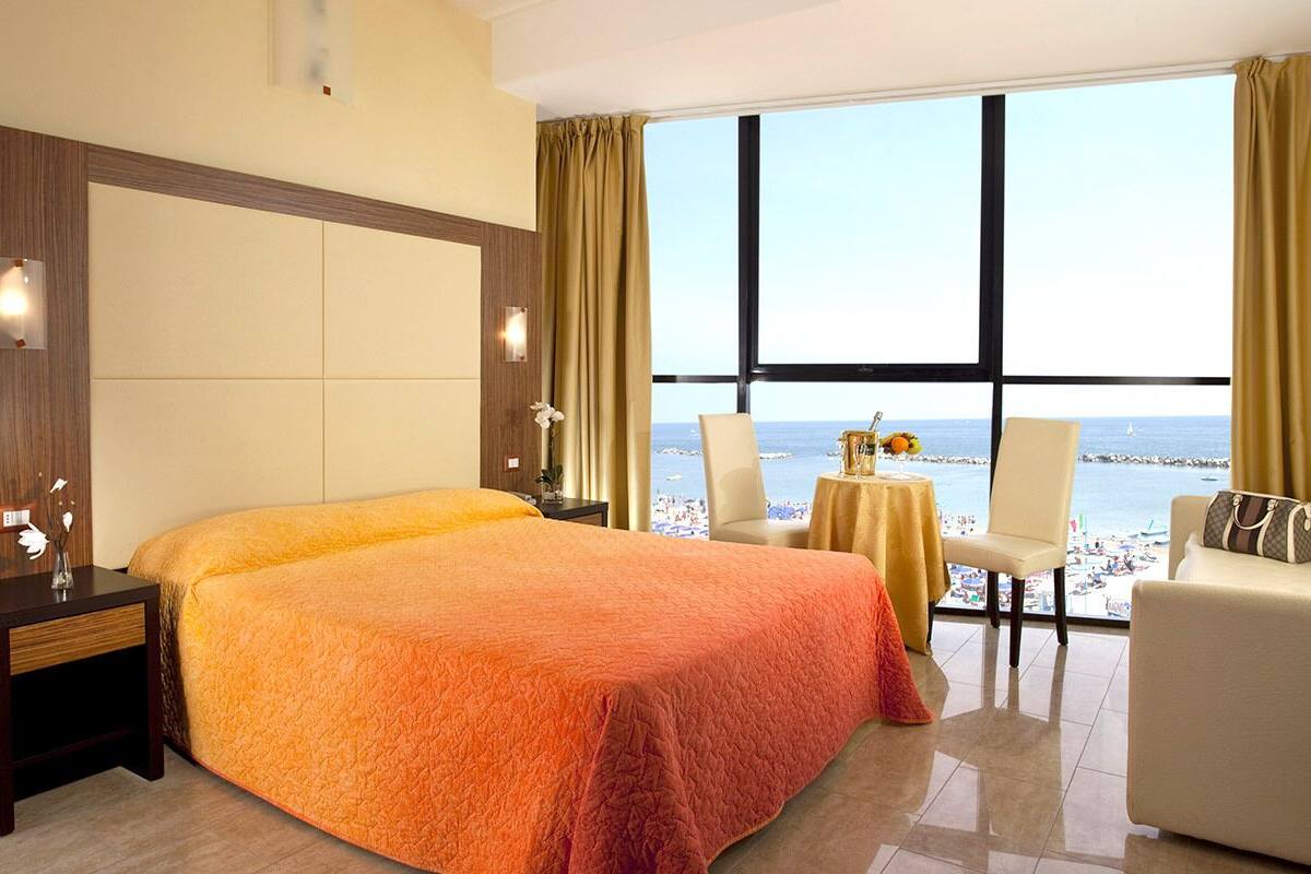 A hotel room with a large bed, a seating area with a view of the sea, and a small table with a vase.