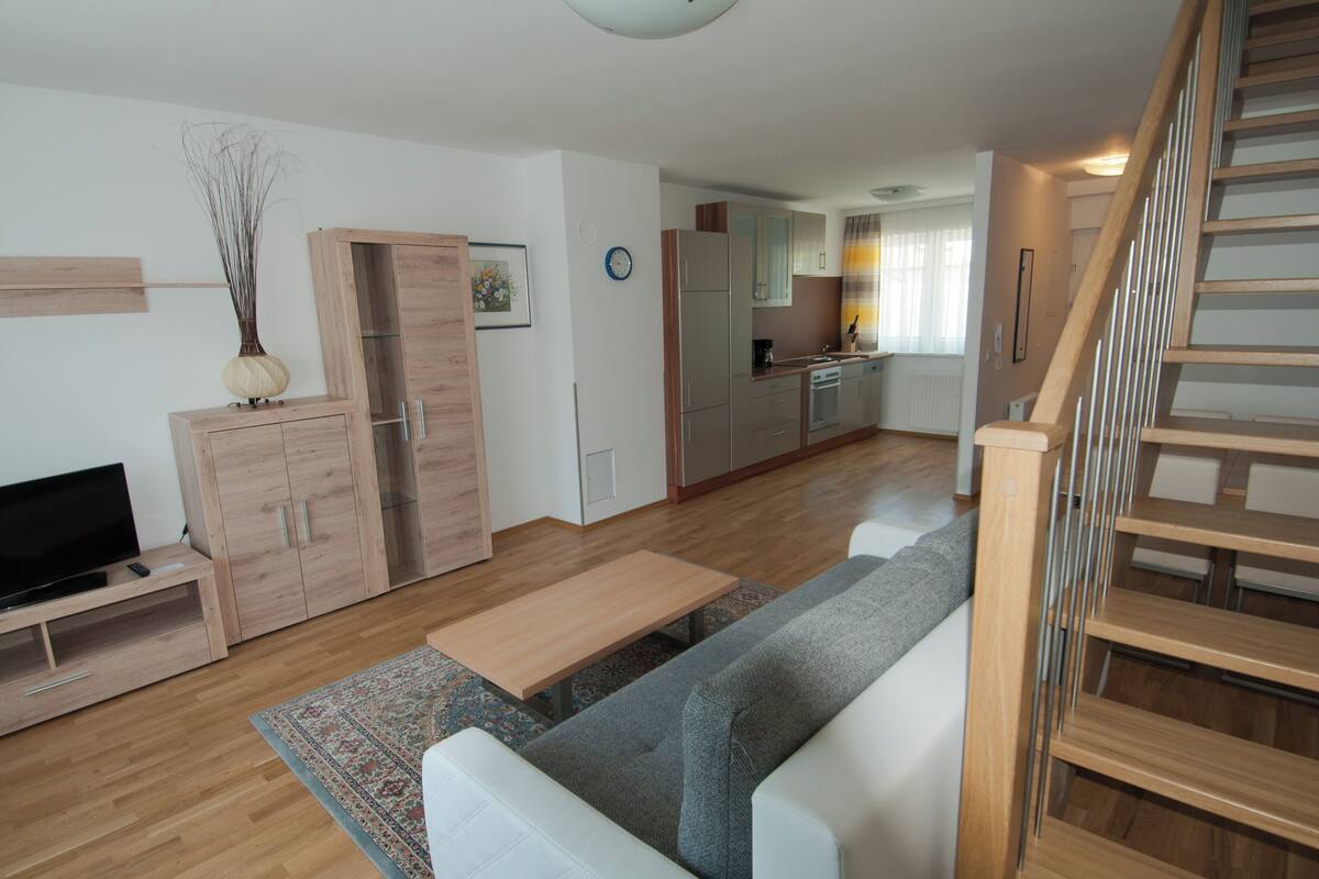A modern living room with a sofa, TV, wooden cabinets, and a kitchen in the background.