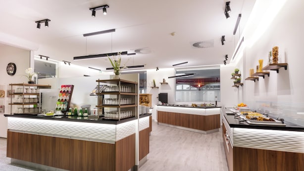 A modern restaurant with wooden counters, shelves with glassware, and a variety of food items displayed.