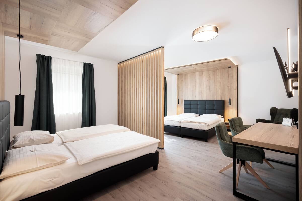 A hotel room with a bed, a desk, a chair, a TV, and a window with curtains.