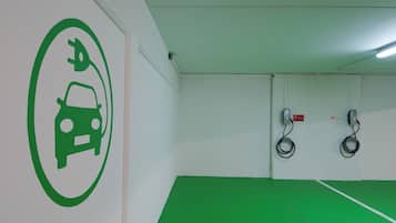 A parking area with a green floor, a wall-mounted electric vehicle charging station, and a green icon indicating the availability of electric vehicle charging.