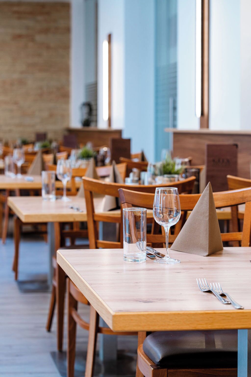 A restaurant with wooden tables and chairs, clear glasses, and a menu stand.