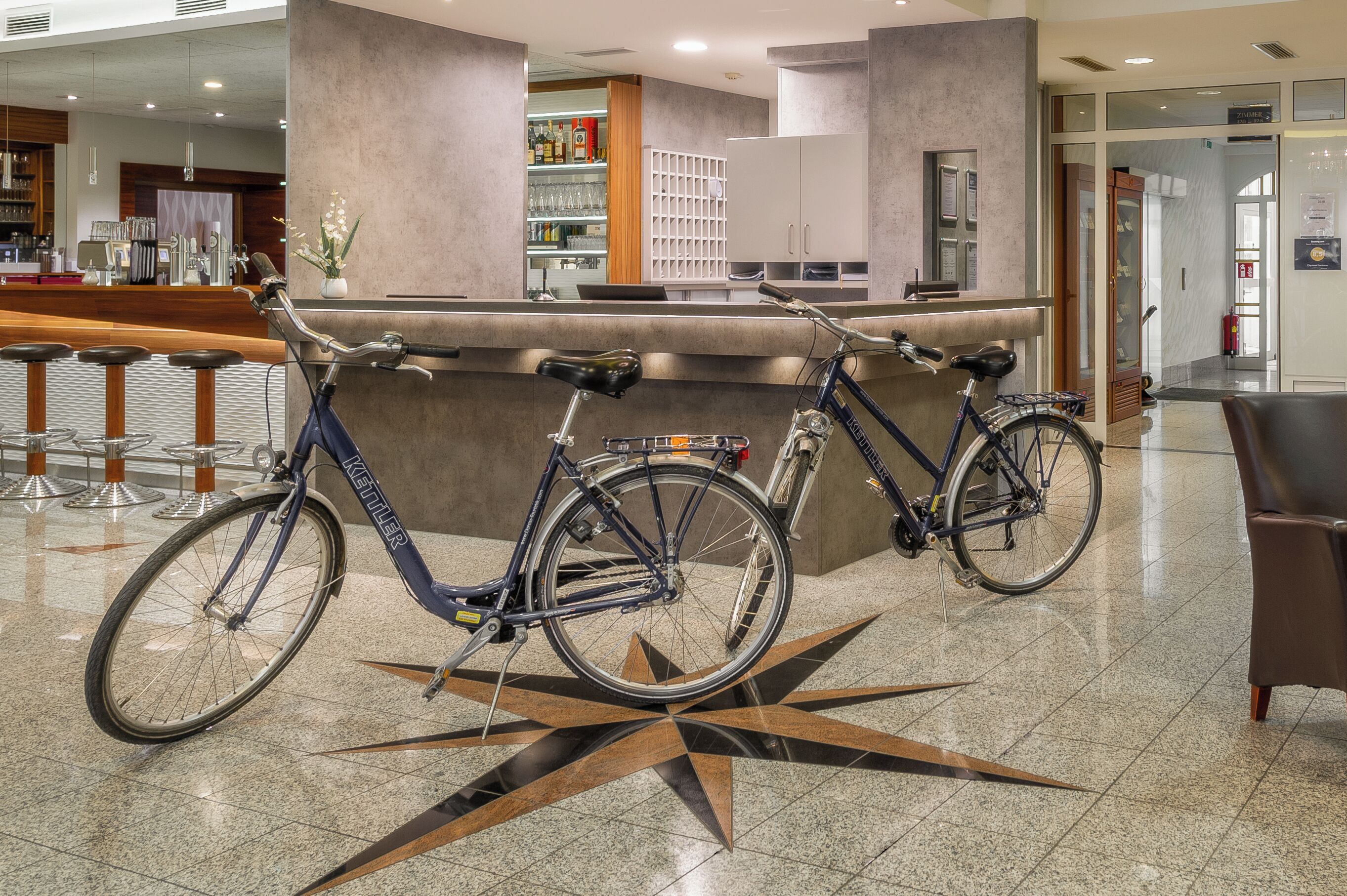 Zona de recepción con diseño de piso en forma de estrella, dos bicicletas, una barra y un área de estar.