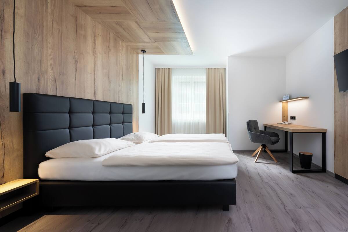 A modern hotel room with a large bed, a desk, and a chair.
