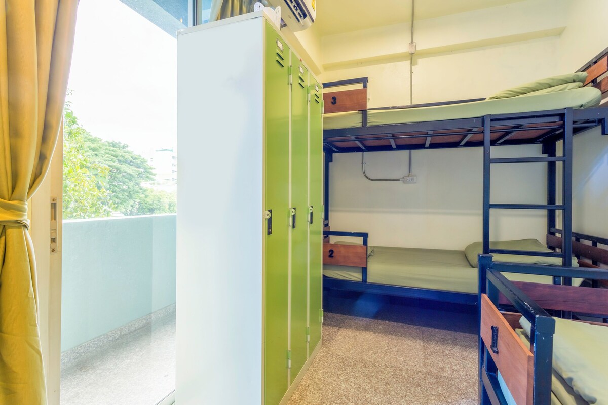 A dormitory room with bunk beds, a green wardrobe, and a small window with curtains.