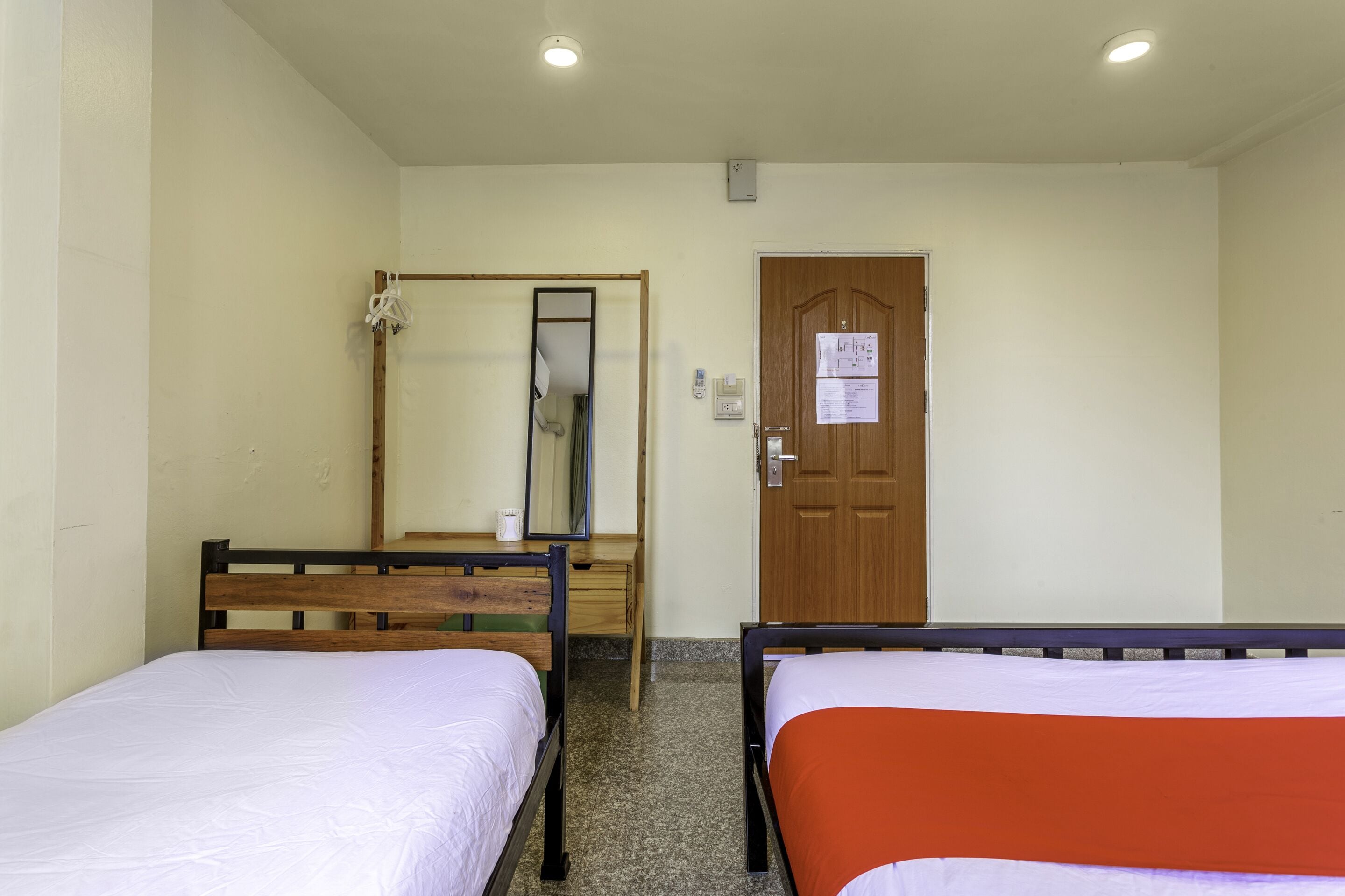 Una habitación con dos camas individuales, una puerta de madera, un espejo y un escritorio pequeño.