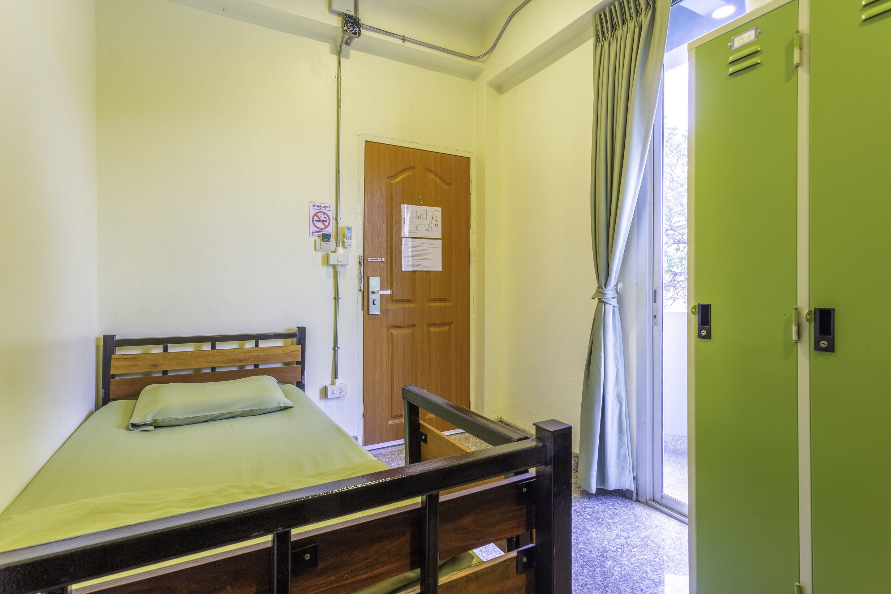 Una habitación con una cama de madera, una puerta verde y una ventana con cortinas.