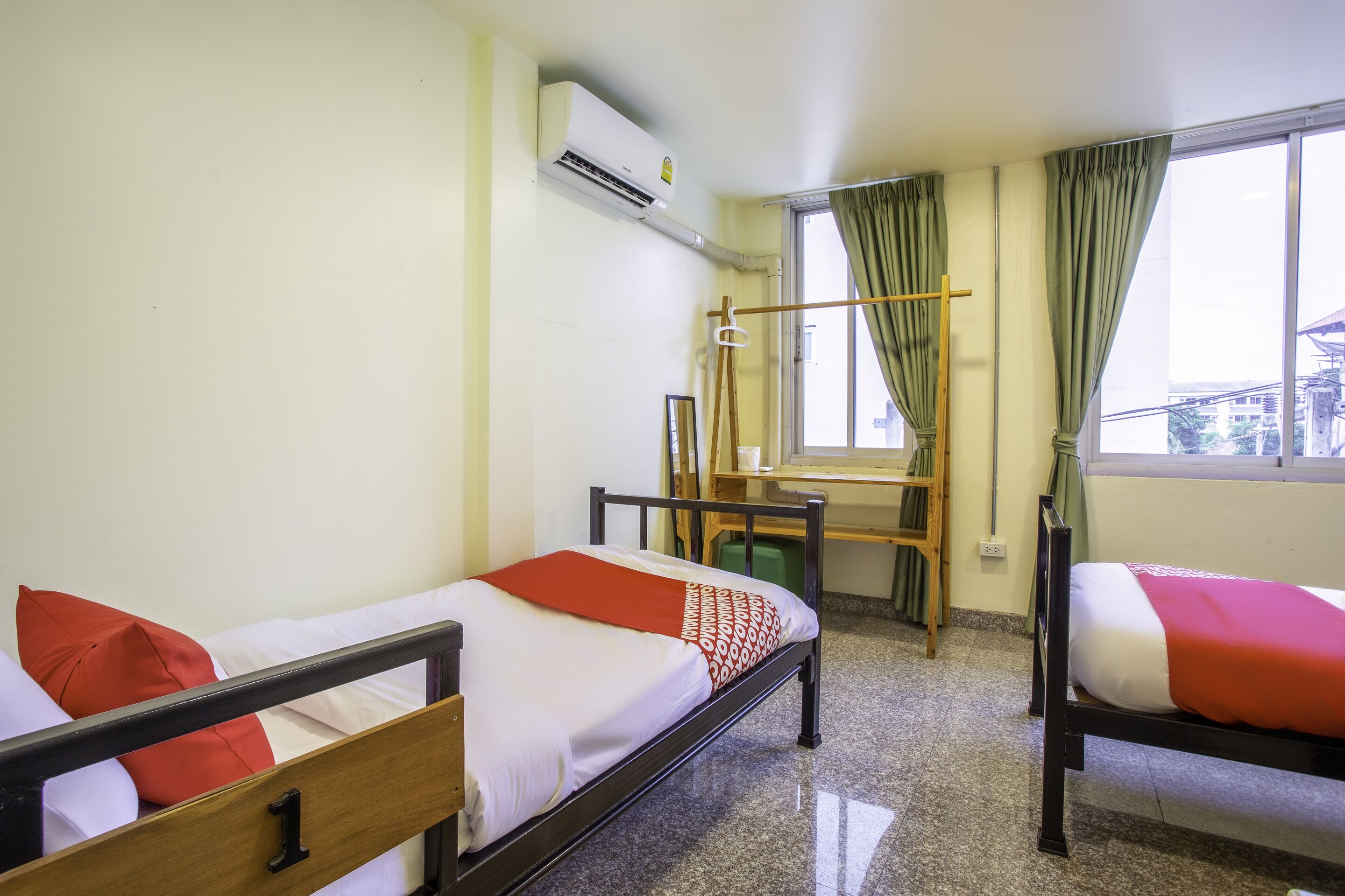 A room with two beds, a window with curtains, an air conditioning unit, and a wooden chair.