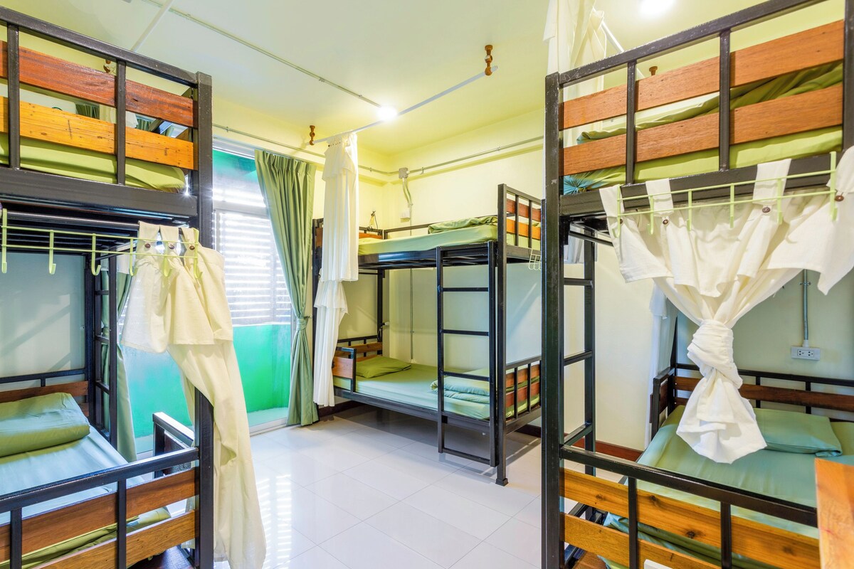 A dormitory room with bunk beds, a window with curtains, and a white wall.