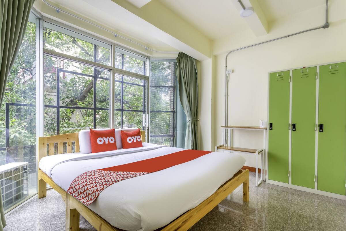 A hotel room with a large bed, green lockers, and a view of trees through the window.
