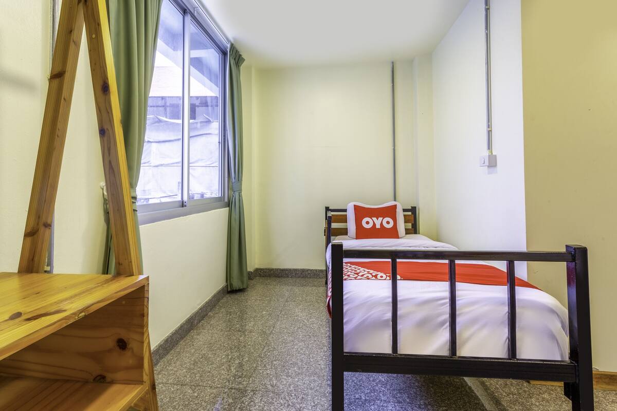 A small, clean room with a bed, a wooden desk, and a window with curtains.