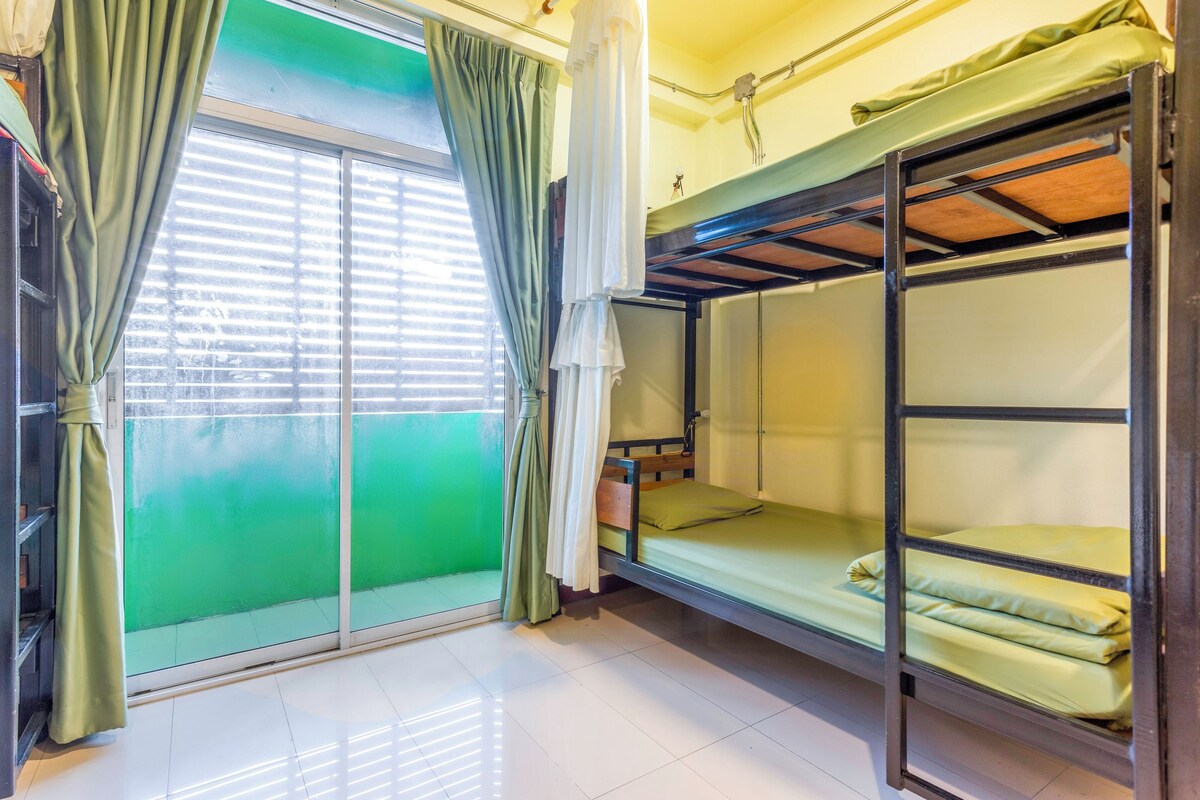 Quarto em dormitório com beliches, porta de correr de vidro e parede externa verde.