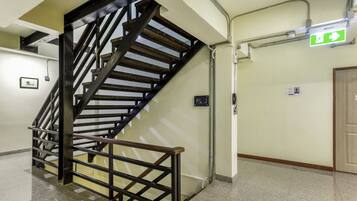 Una escalera con barandilla metálica, un letrero de salida de emergencia verde y una puerta con marco de madera.