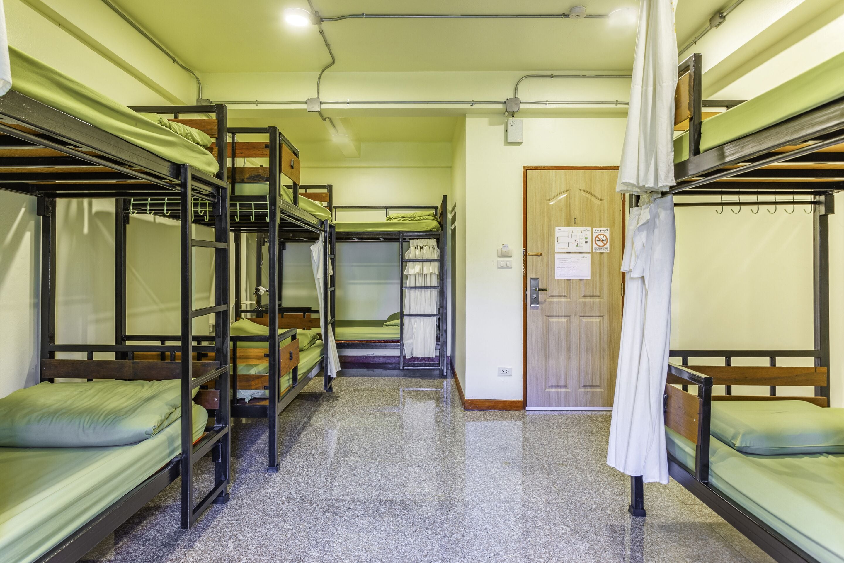 A dormitory room with bunk beds, a wooden door, and a tiled floor.