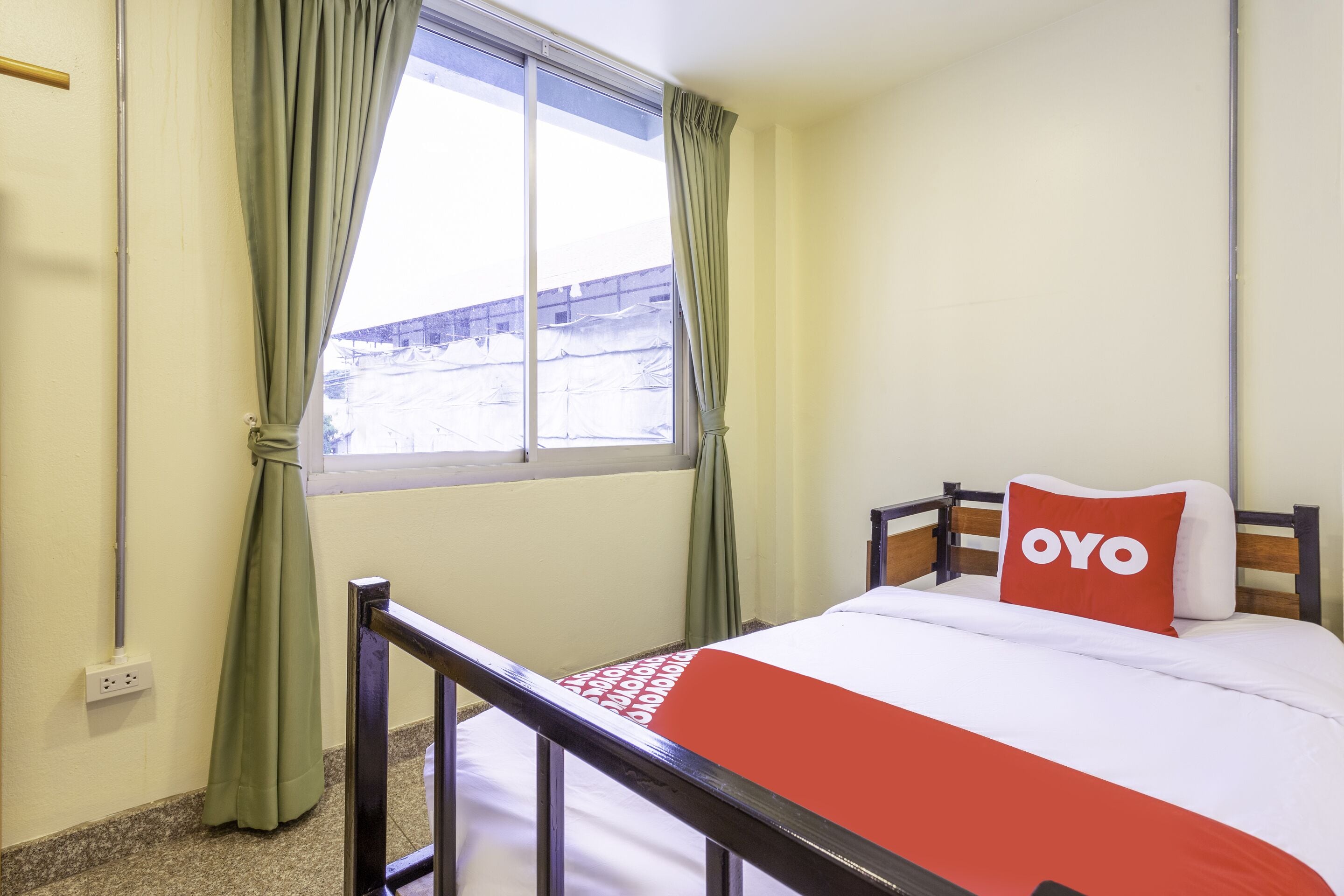 A single bed with a red and white bedspread and a pillow labeled "OYO".