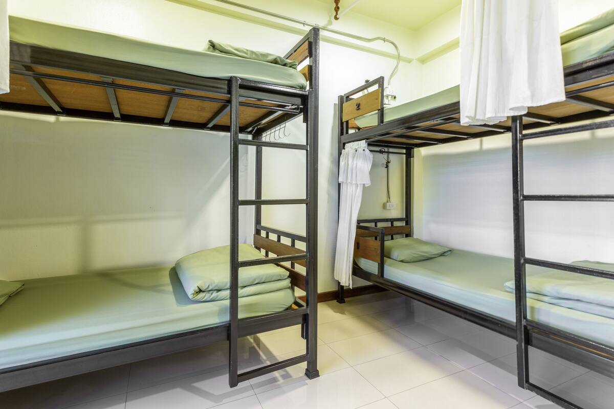 A dormitory room with bunk beds, a ladder, and a hanging light fixture.