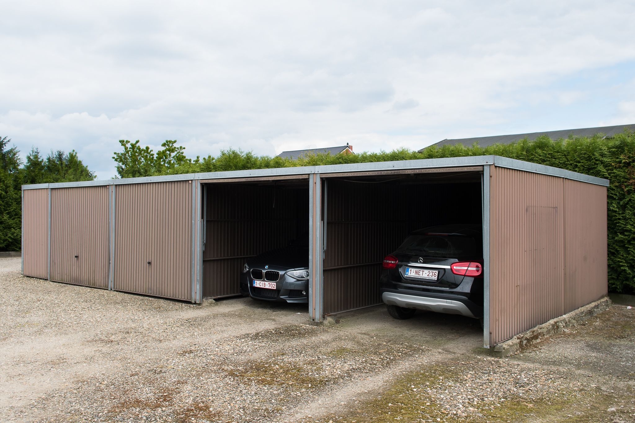 Un bâtiment en métal doté de deux grandes portes de garage ouvertes, chacune abritant une voiture.