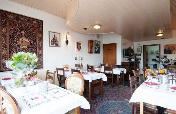A dining area with wooden tables and chairs, a large decorative rug, and wall-mounted artwork.