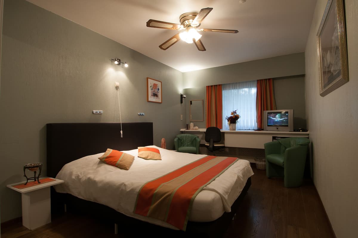 Ein Hotelzimmer mit Bett, Schreibtisch, Stuhl, Fernseher und Deckenventilator.