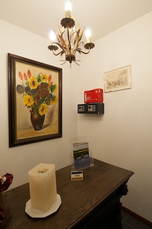 A room with a chandelier, a framed painting of sunflowers, a candle, a small table with a vase, and a framed picture on the wall.