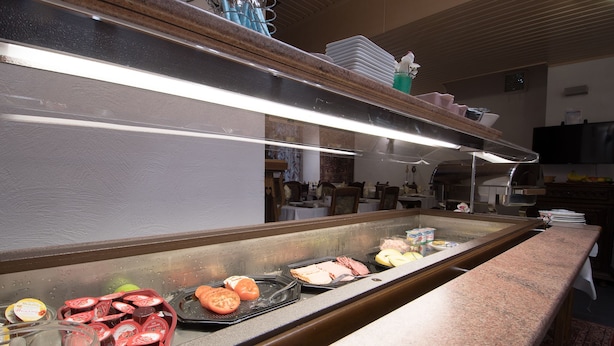 A buffet counter with various food items and a glass display case. - Hotel Apollo (Zutendaal)