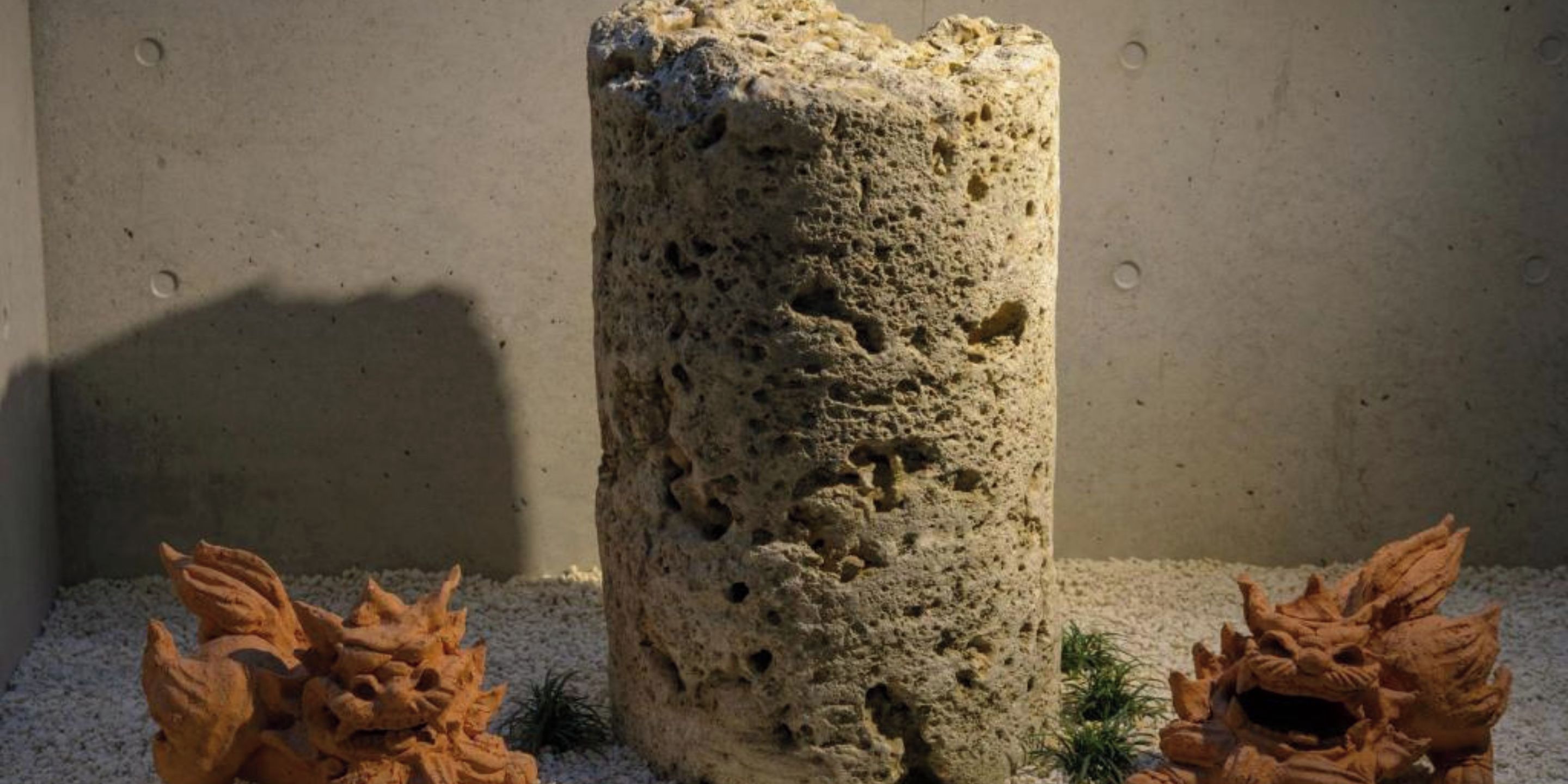 Un pilar de piedra texturizado con superficie rugosa y agujeros, rodeado de pequeños detalles decorativos.