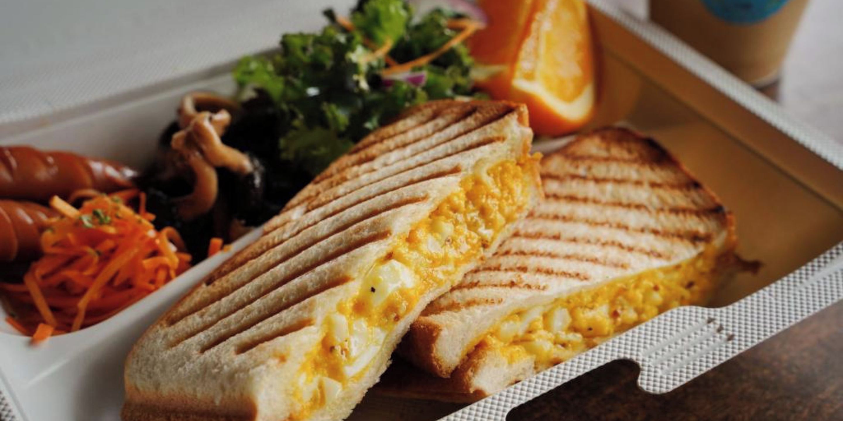 A grilled sandwich with egg inside, accompanied by a side salad and sliced orange.