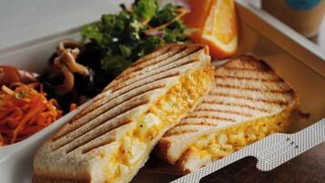 A grilled sandwich with egg inside, accompanied by a side salad and sliced orange.