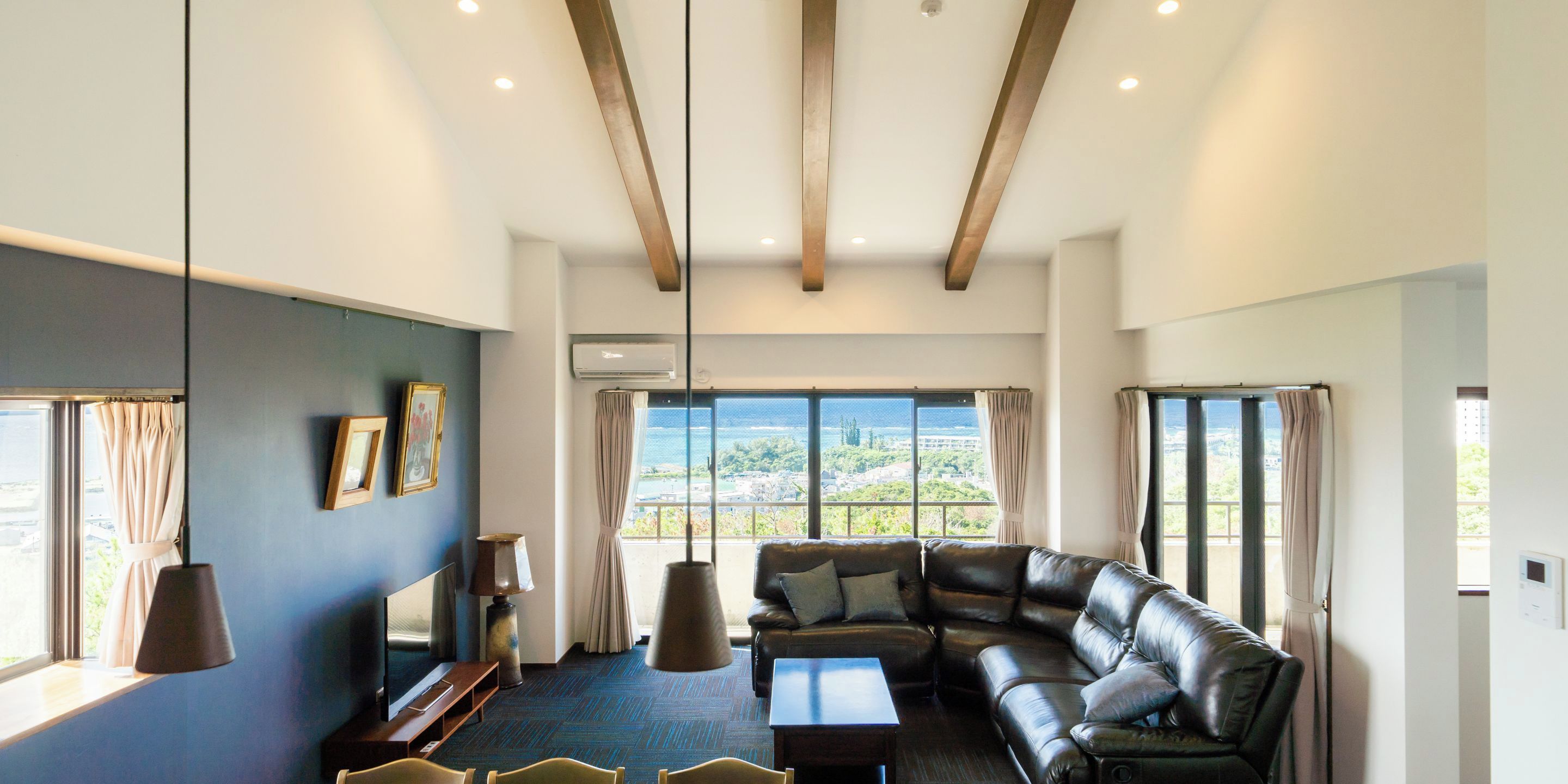 A modern living room with a leather sofa, a flat-screen TV, and a large window offering a view of the sea.
