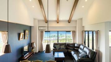 A modern living room with a leather sofa, a flat-screen TV, and a large window offering a view of the sea.