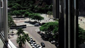 A view from a window overlooking a parking lot with cars, a road, and a mountain. - Aconchego Frente Mar (Rio de Janeiro)