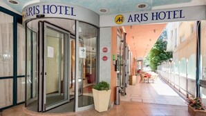 L’extérieur de l’hôtel Aris se distingue par son entrée avec porte tournante, son espace extérieur aménagé et abrité, et sa vue sur la rue.