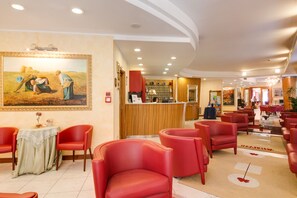 A hotel lobby with red chairs, a reception desk, and a large painting on the wall.