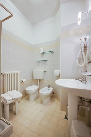 A bathroom with a toilet, bidet, radiator, and a sink.